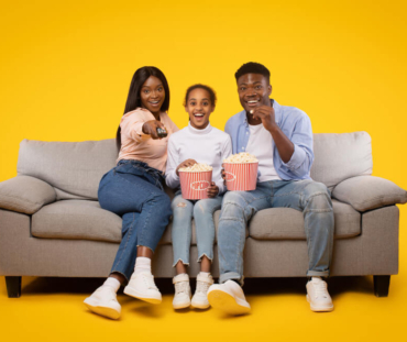 joyful-black-family-three-sitting-sofa-watching-movie-eating-popcorn-from-bucket-isolated-yellow-wall (1)