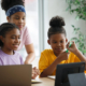 portrait-brilliant-black-girl-with-braces-writes-exercise-notebook-smiles-junior-classroom-with-diverse-group-children-learning-new-stuff